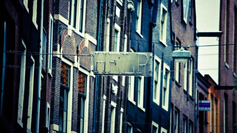 help sign hanging across a street and two lines of buildings
